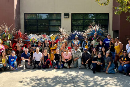 large group of people smiling with some dressed in feathered head dresses