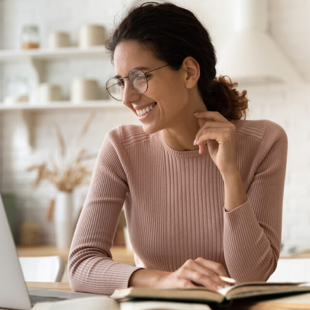 woman in sweater smiling at laptop