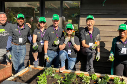 group of people smiling wearing green hats by a raised flower bed