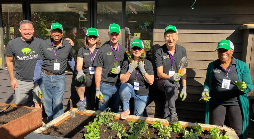 group of people smiling wearing green hats by a raised flower bed