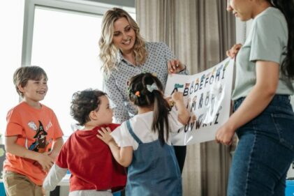 Two elementary school teachers hold a poster up in class for their young students to look at.