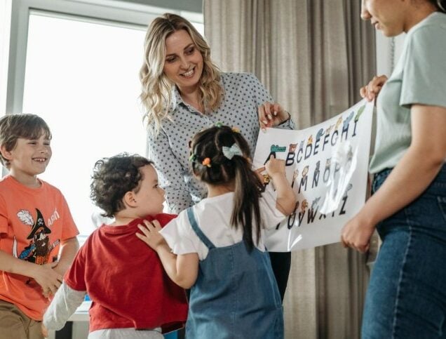 Two elementary school teachers hold a poster up in class for their young students to look at.