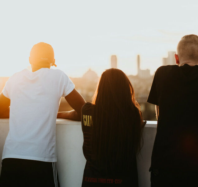 Four young adults stand on a rooftop, watching a sunrise with their backs to the camera.