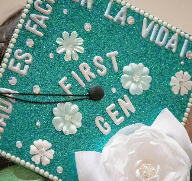 A college graduate's mortar board is decorated with green glitter and white flowers.
