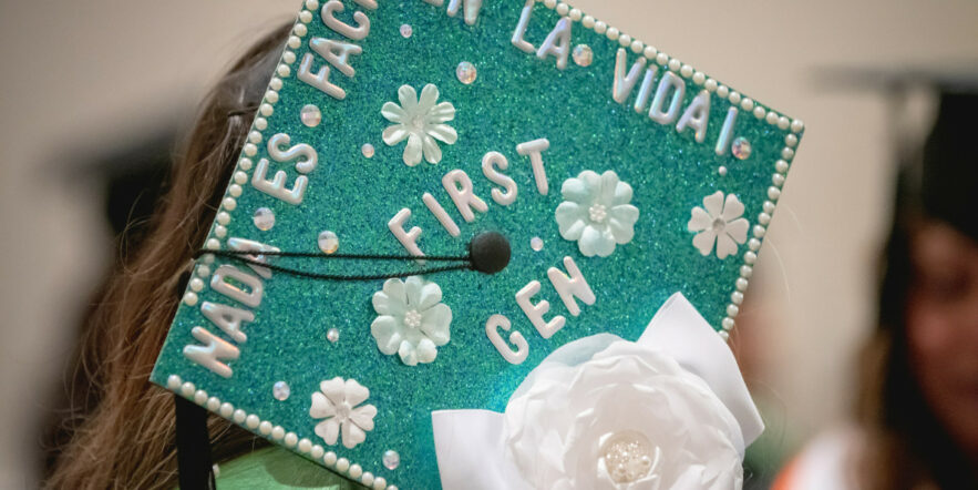 A college graduate's mortar board is decorated with green glitter and white flowers.