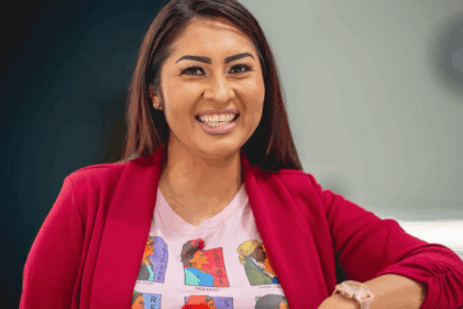 A woman wearing a white graphic T-shirt under a red sweater smiles for the camera.