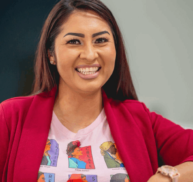 A woman wearing a white graphic T-shirt under a red sweater smiles for the camera.