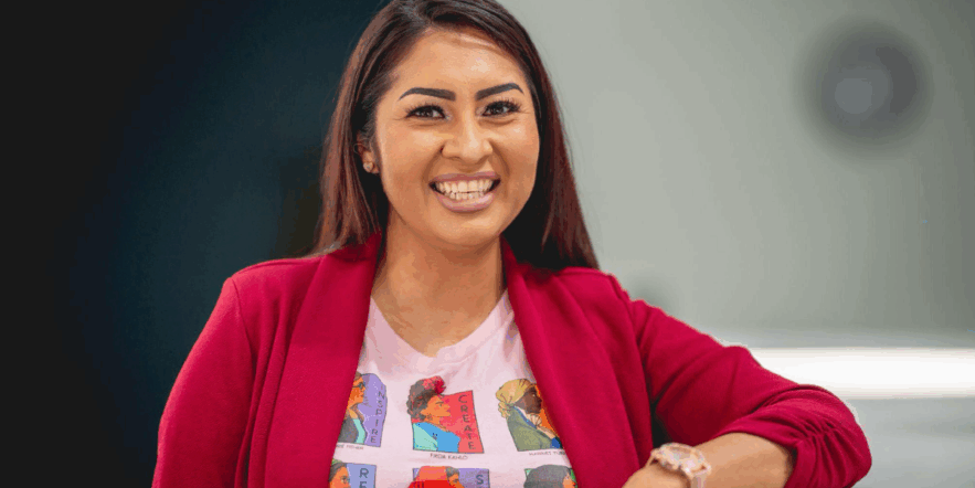 A woman wearing a white graphic T-shirt under a red sweater smiles for the camera.