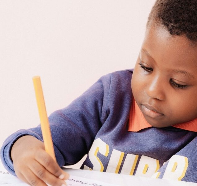 Small child writing in a notebook with a pencil.