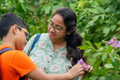 Woman shows flower to young child with backpack.