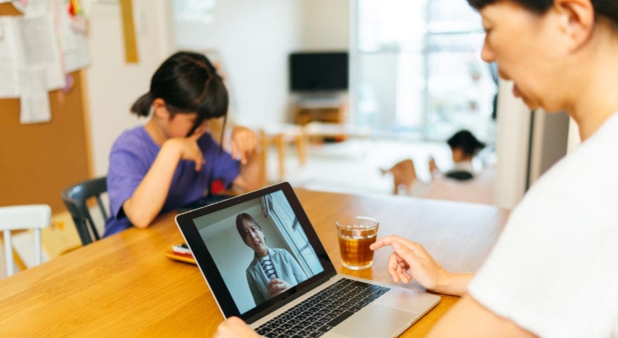 mother utilizing telehealth with child in background