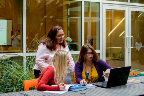 3 women outside looking at a laptop