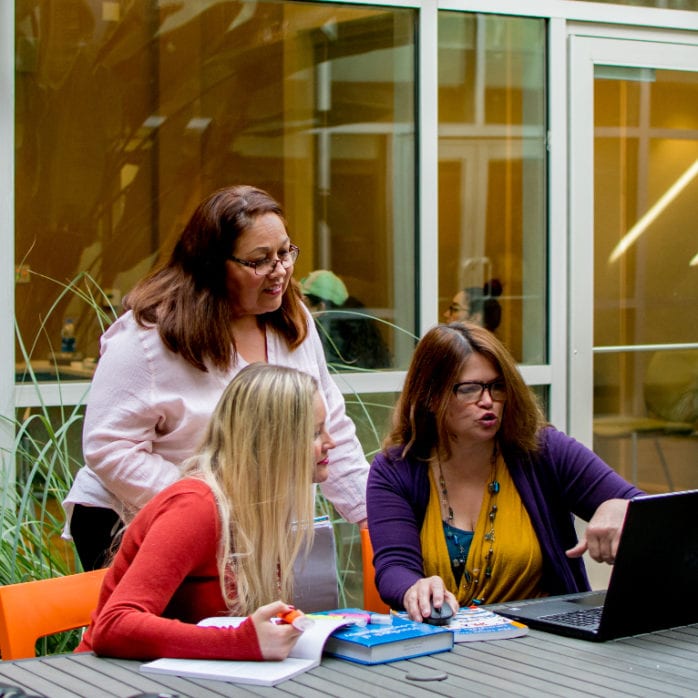 3 women outside looking at a laptop