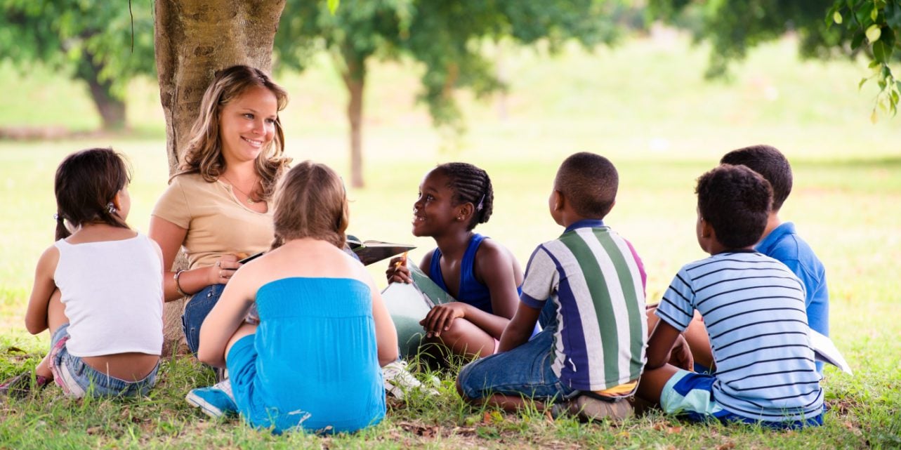 woman leaning against tree, children sitting around her