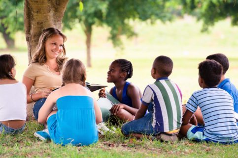woman leaning against tree, children sitting around her