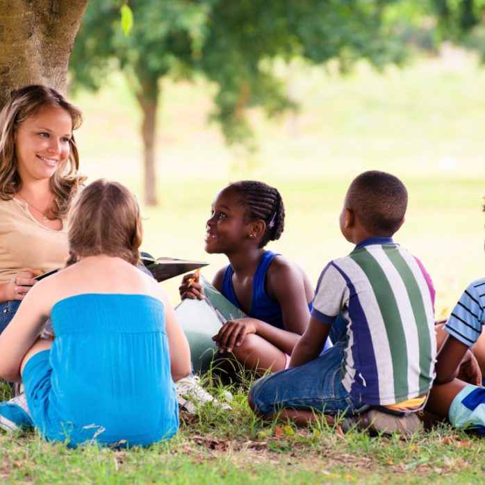 woman leaning against tree, children sitting around her