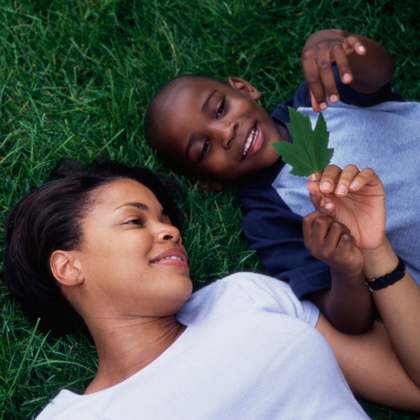 Woman and boy laying in grass smiling looking at a leaf in the boy's hand