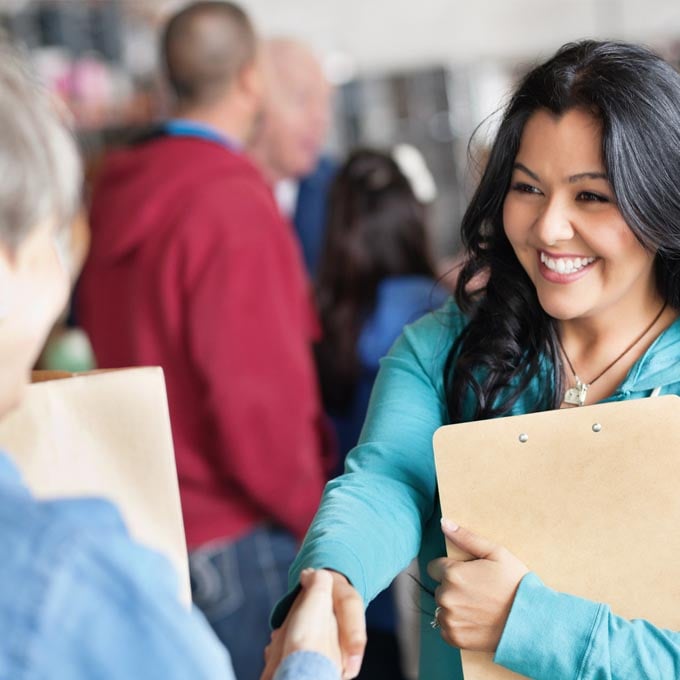 smiling woman shaking hands while holding a clipboard