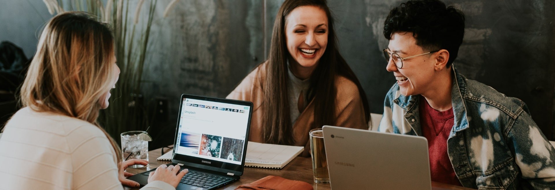three students laughing with one typing on laptop